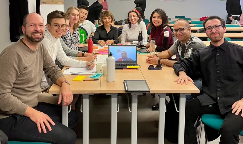 Georg Fischer sitzt mit einer internationalen Studierendengruppe an einem Tisch voller Arbeitsmaterialien.
